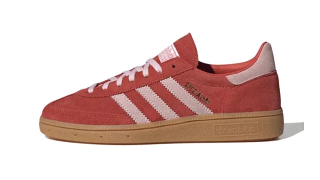 Een felrode suède sneaker met witte Adidas-strepen, witte veters en een rubberen zool. De schoen is voorzien van de tekst "SPEZIAL" op de zijkant en een Adidas-logo op de hiel, dat doet denken aan de klassieke Adidas Handball Spezial Bright Red/Clear Pink van Adidas.