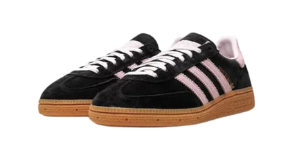 Een paar zwarte lage sneakers met roze strepen en een bruine rubberen zool, die doet denken aan de klassieke Adidas Handball Spezial Core Black Clear Pink.